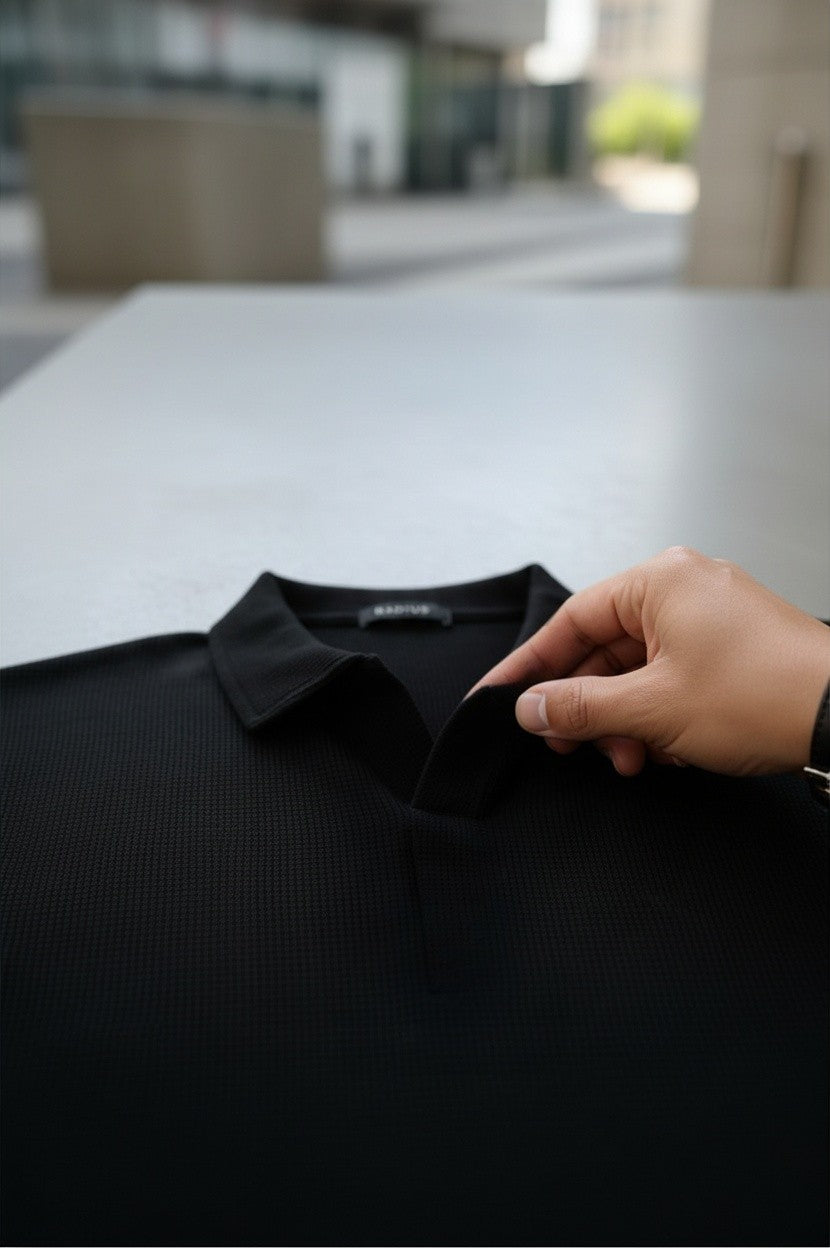 RADIUS Obsidian black waffle-knit polo shirt with a textured fabric and button placket held by a hand.