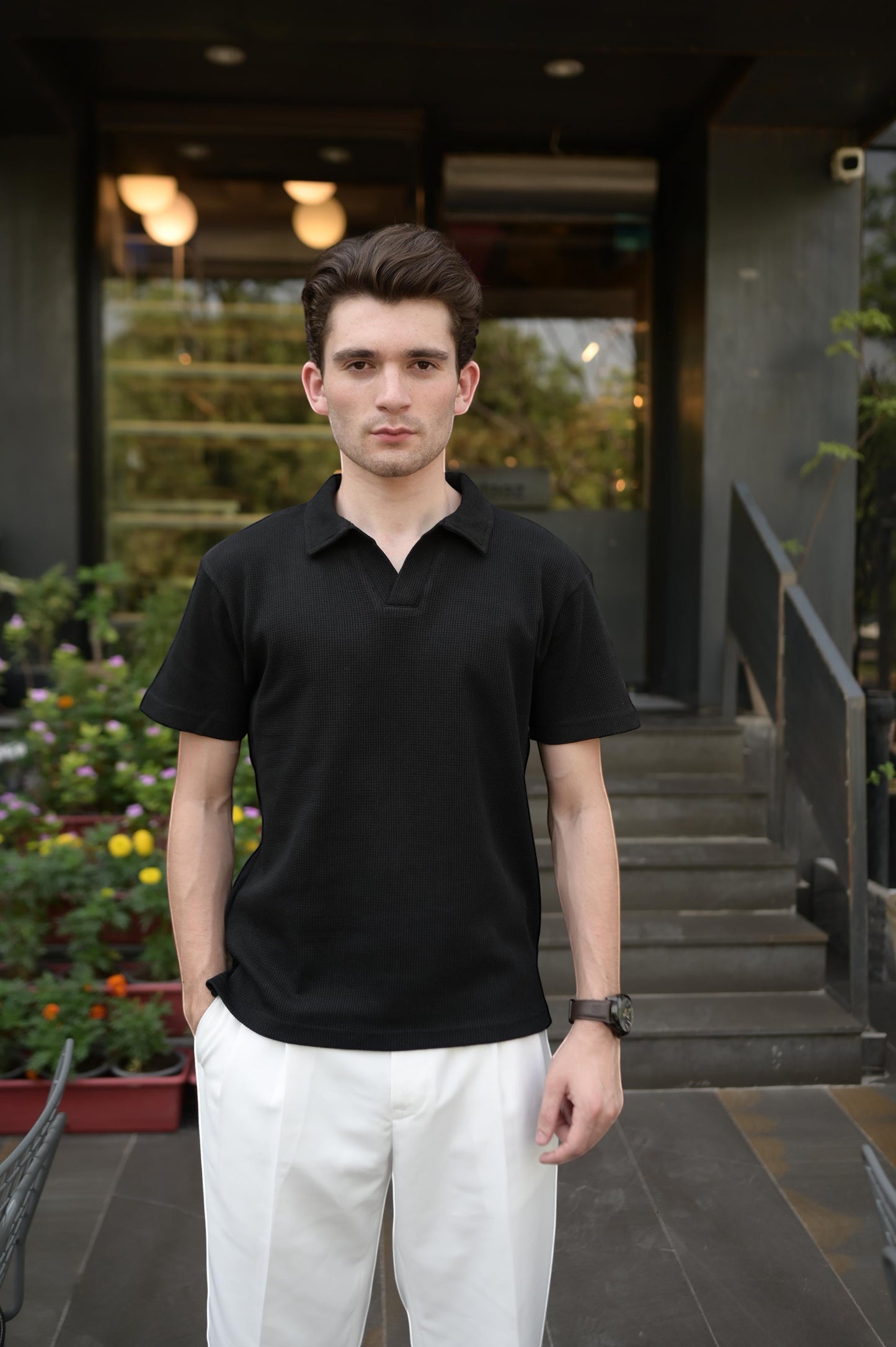 RADIUS model wearing a black waffle-knit polo with a placket-less V-neck and dropped shoulders, paired with white pants.