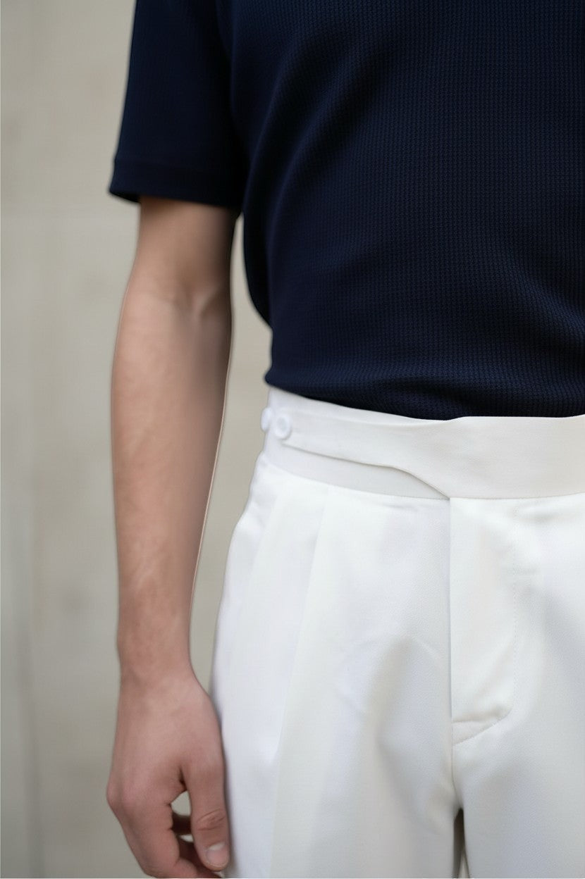 RADIUS white Gurkha trousers with a high-waisted dual-button closure and sharp pleats, paired with a navy polo shirt.