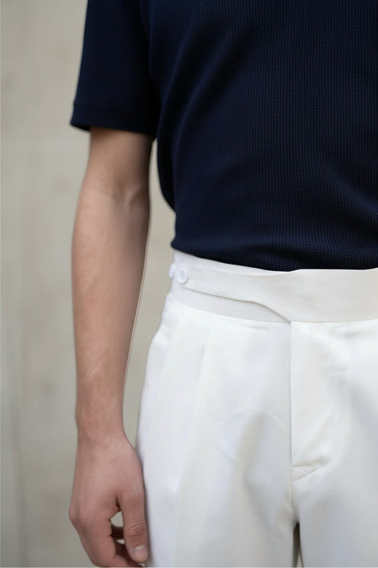 RADIUS white Gurkha trousers with a high-waisted dual-button closure and sharp pleats, paired with a navy polo shirt.